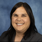 headshot of a smiling woman with shoulder-length dark hair in a charcoal grey suit